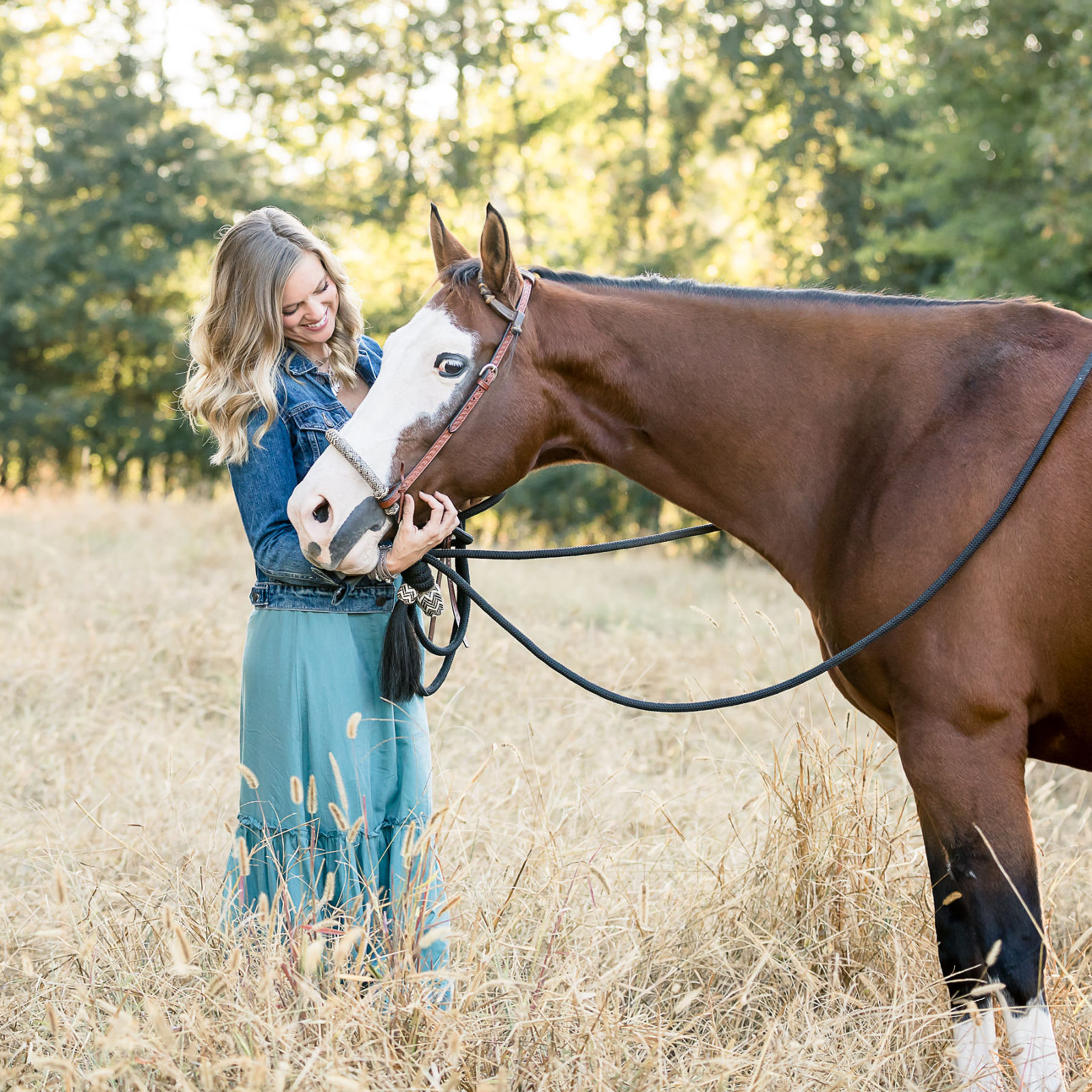 smiling lady teal dress denim jacker with overo paint mare in golden field