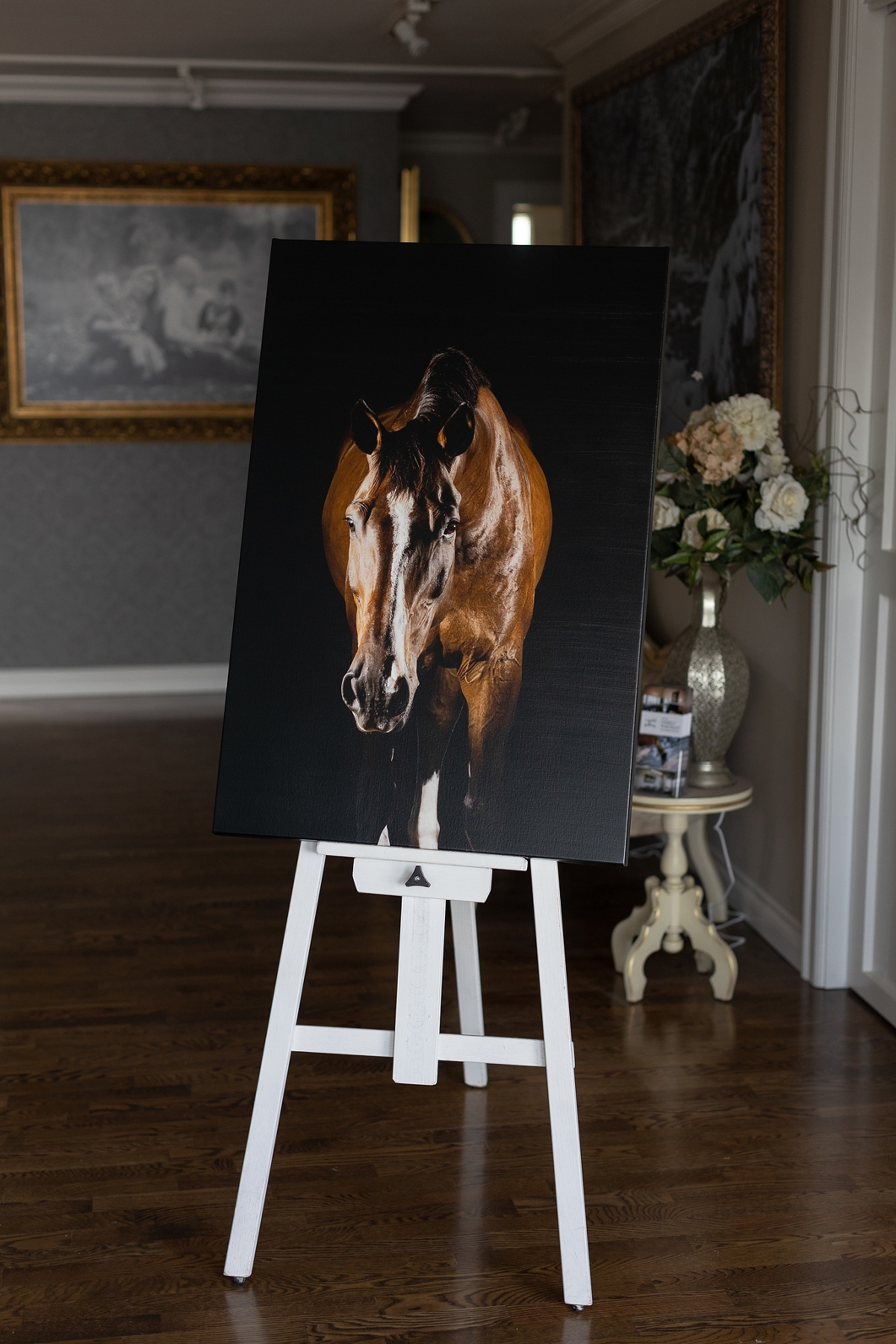 A painting of a horse displayed on a white easel in a room with elegant decor.