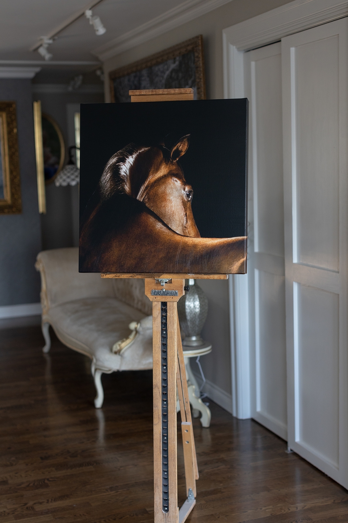 A painting of a horse displayed on an easel in an elegantly furnished room.