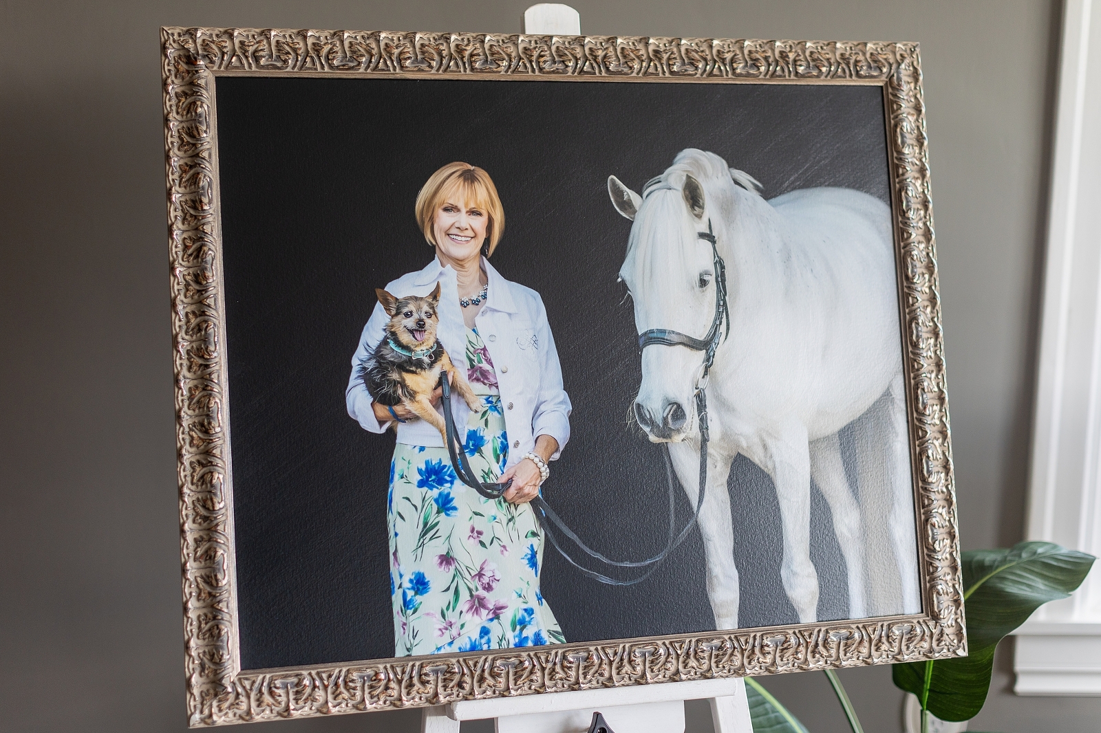 A framed photograph of a smiling woman holding a dog, standing next to a white horse.