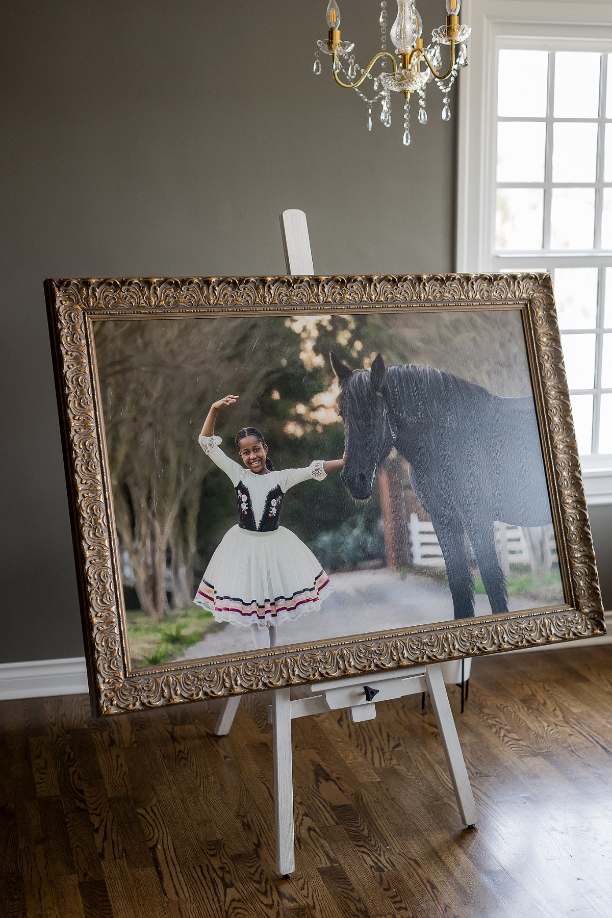 Girl smiling at a horse, both framed and displayed on an easel in a room with elegant decor.